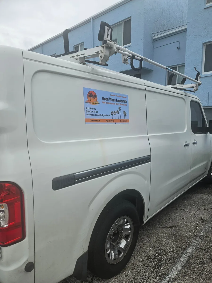 White Good Vibes Locksmith work van with a roof rack and door magnet parked outside a building