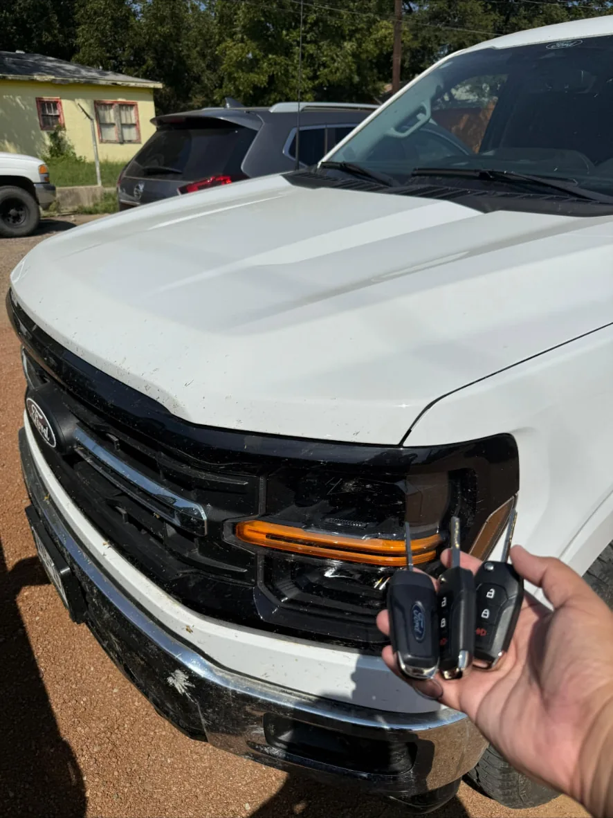 Hand holding two newly cut and programmed Ford remote key fobs in front of a white Ford pickup truck