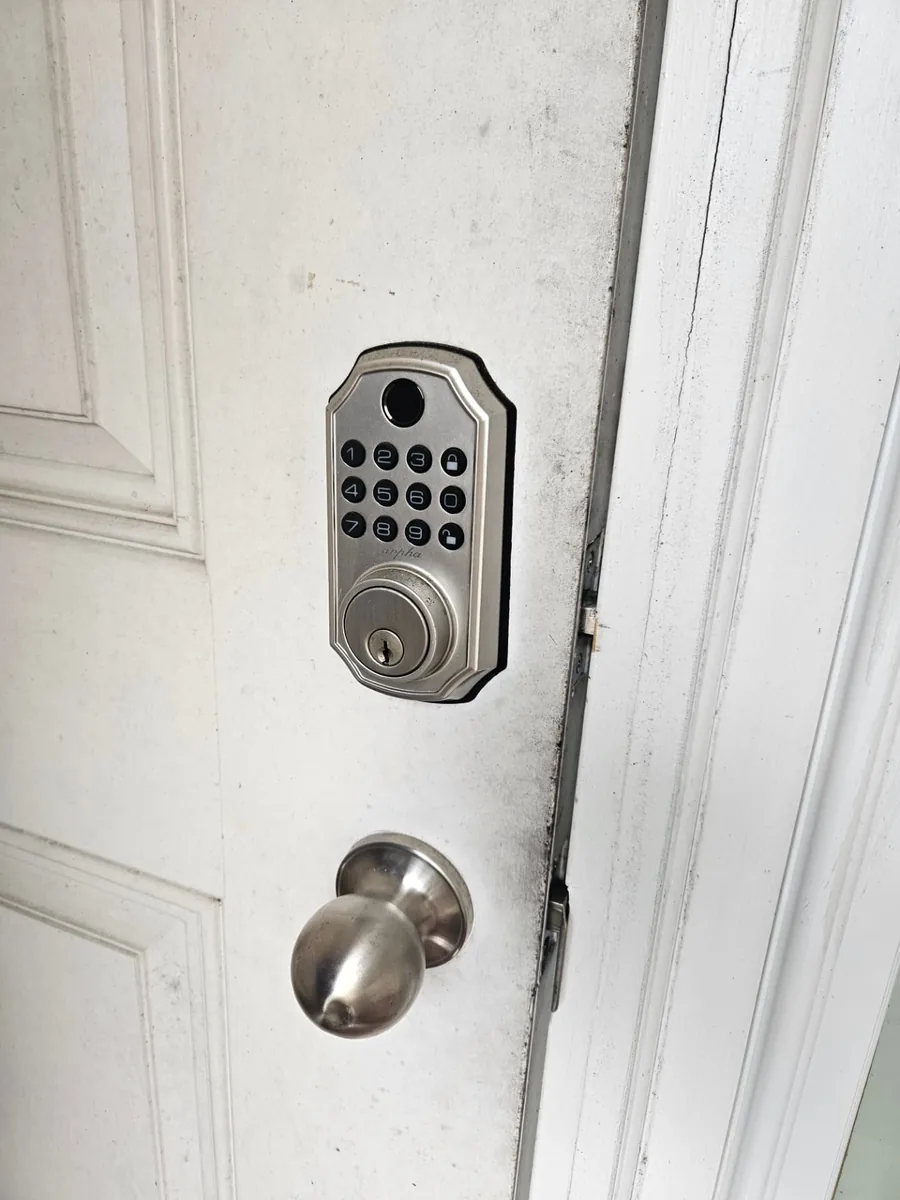 Brushed nickel keypad deadbolt with fingerprint reader installed above a knob on a white door